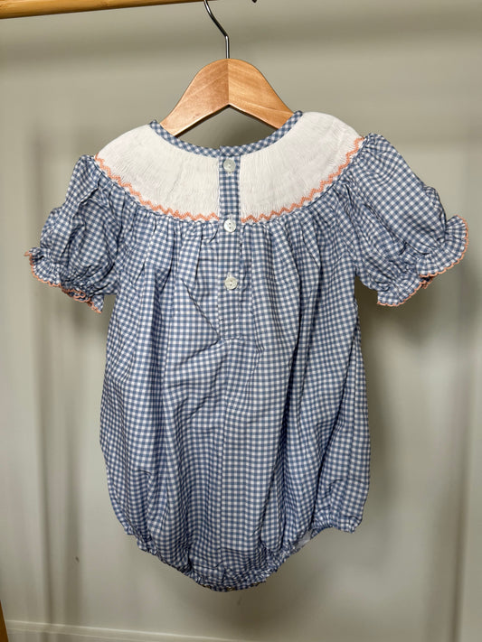 Blue checkered baby romper with white collar on a wooden hanger against a beige wall.