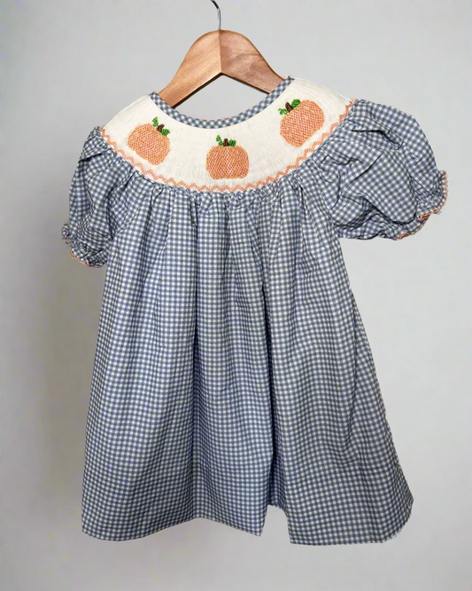 Blue checkered dress with pumpkin embroidery on a hanger against a neutral background