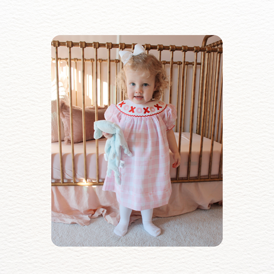 Child in a pink dress standing in front of a crib with a white background