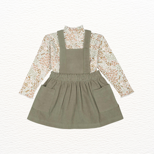 Green overall dress with floral blouse on a white background