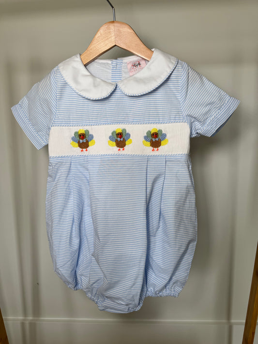 Baby romper with blue and white striped pattern and embroidered turkeys on a hanger against a beige wall.